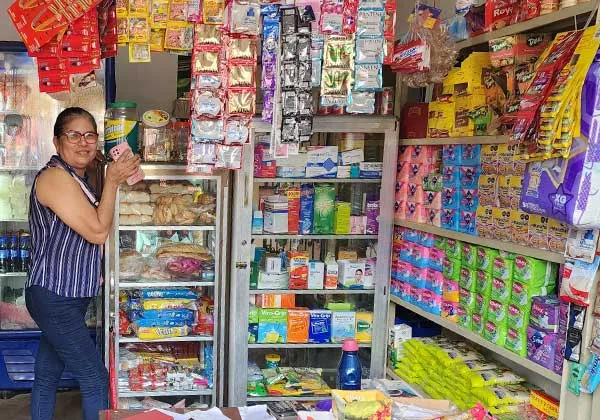 Mujer atendiendo un pequeño negocio con productos en estantes.